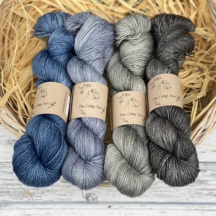 Four skeins of yarn in shades of blue and grey.