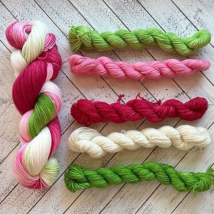 A large skein of yarn and five small skeins of yarn in shades of green, pink, red and white.