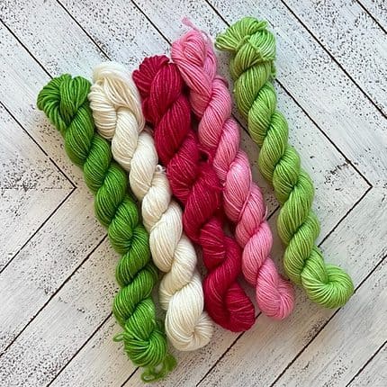 Five skeins of yarn in red, pink, white, light green, and medium green.
