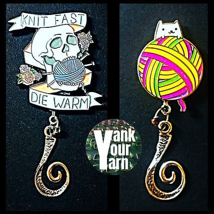 A pair of knitting badges featuring magnetic backs and hanging hooks. One is an image of a skull with the words Knit Fast, Die Warm. The other is an image of a large multicolored ball of yarn, with a white cat peeking over the top.
