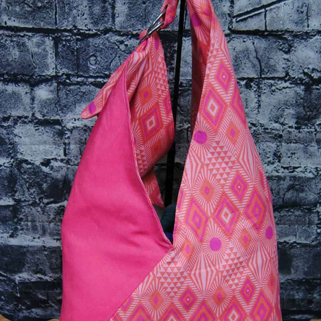A bento project bag in half plain pink fabric and half with a diamond pattern.