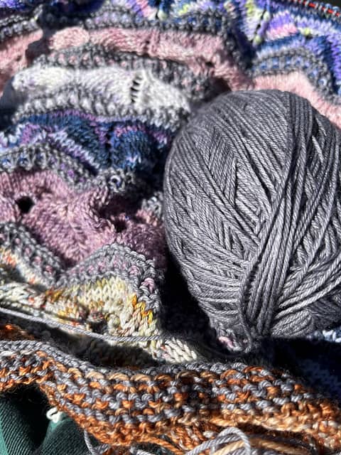 A purple, blue and gray shawl and a ball of gray yarn.