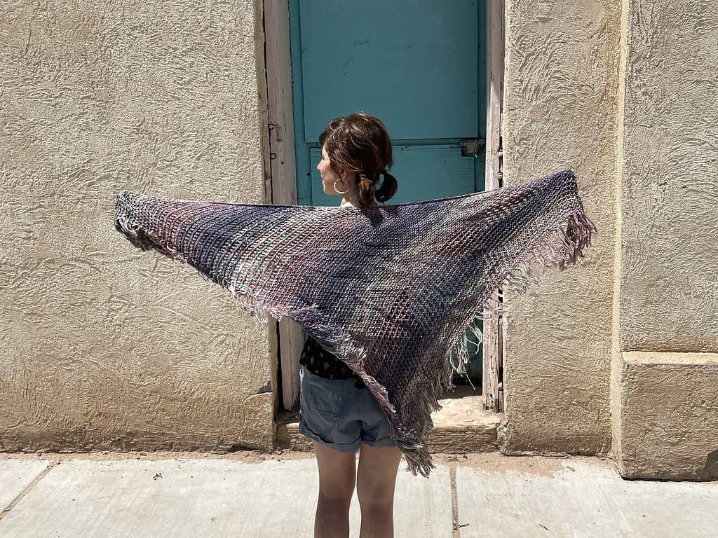 A woman holding up a purple and blue shawl.