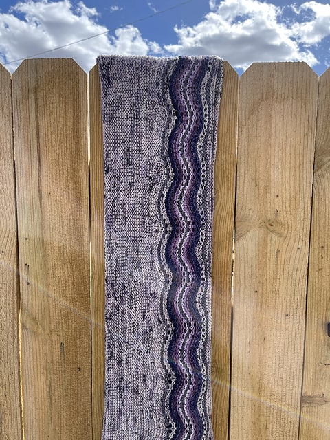 A gray and purple cowl hanging on a fence.