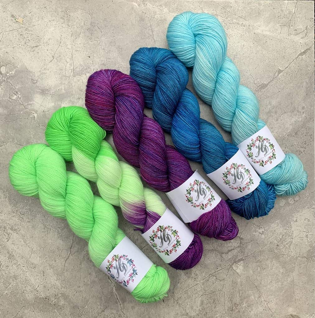 Bright Kelly green yarn, variegated bright green and magenta yarn, deep magenta purple yarn, deep cerulean blue yarn, and sky blue yarn.