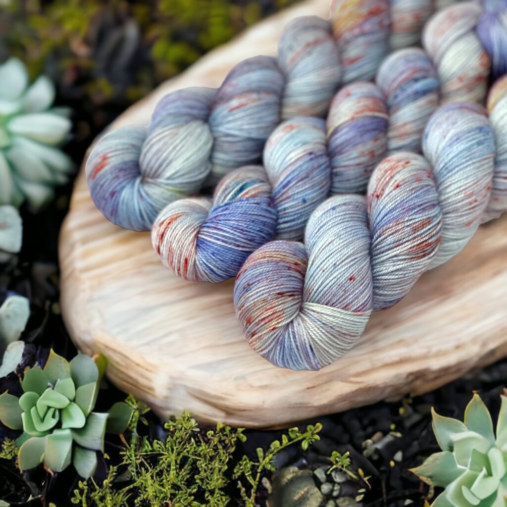Three skeins of light blue yarn in a wooden tray surrounded by succulents.