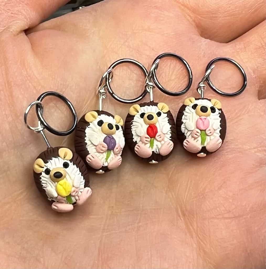 Four hand sculpted hedgehogs - each holding a different colored tulip (yellow, purple, pink, and red).