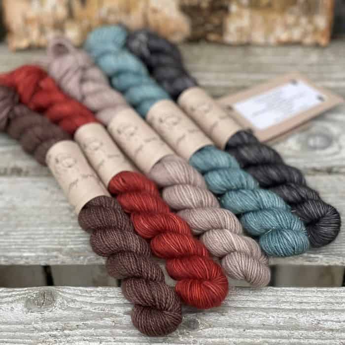 Five mini skeins. From left to right: a brown skein, a red skein, a light brown skein, a teal skein and a dark grey skein.