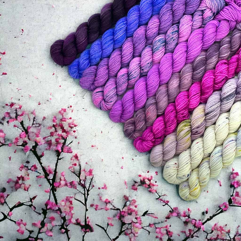 An array of ten mini skeins of yarn in varying shades of purple flanked by cherry blossoms.