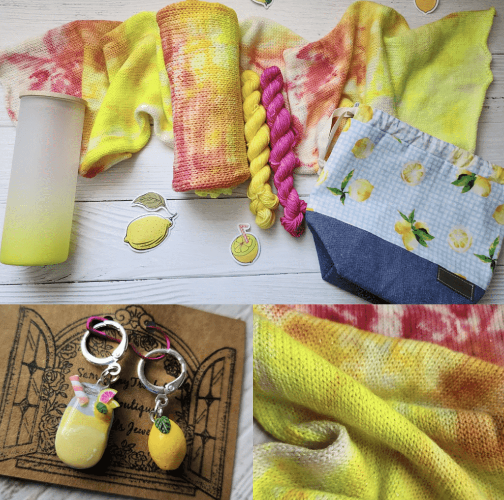 A pink lemonade (pink and yellow) sock blank laying atop another sparkle blank spread outvon a white wooden background. The sock blanks are surrounded by a lemon and jean fabric project bag, lemonade in a mason jar and lemon charms, a yellow frosted tumbler with a bamboo lid, lemon stickers, and yellow and pink mini skeins.