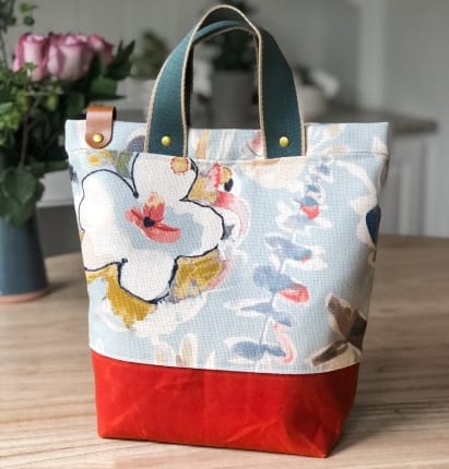 A floral print and red project bag with a green handle.