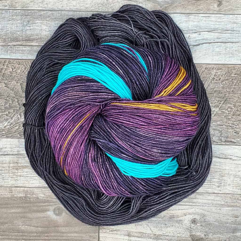 A skein of self-striping yarn coiled up and surrounded by a smaller charcoal gray skein of yarn.