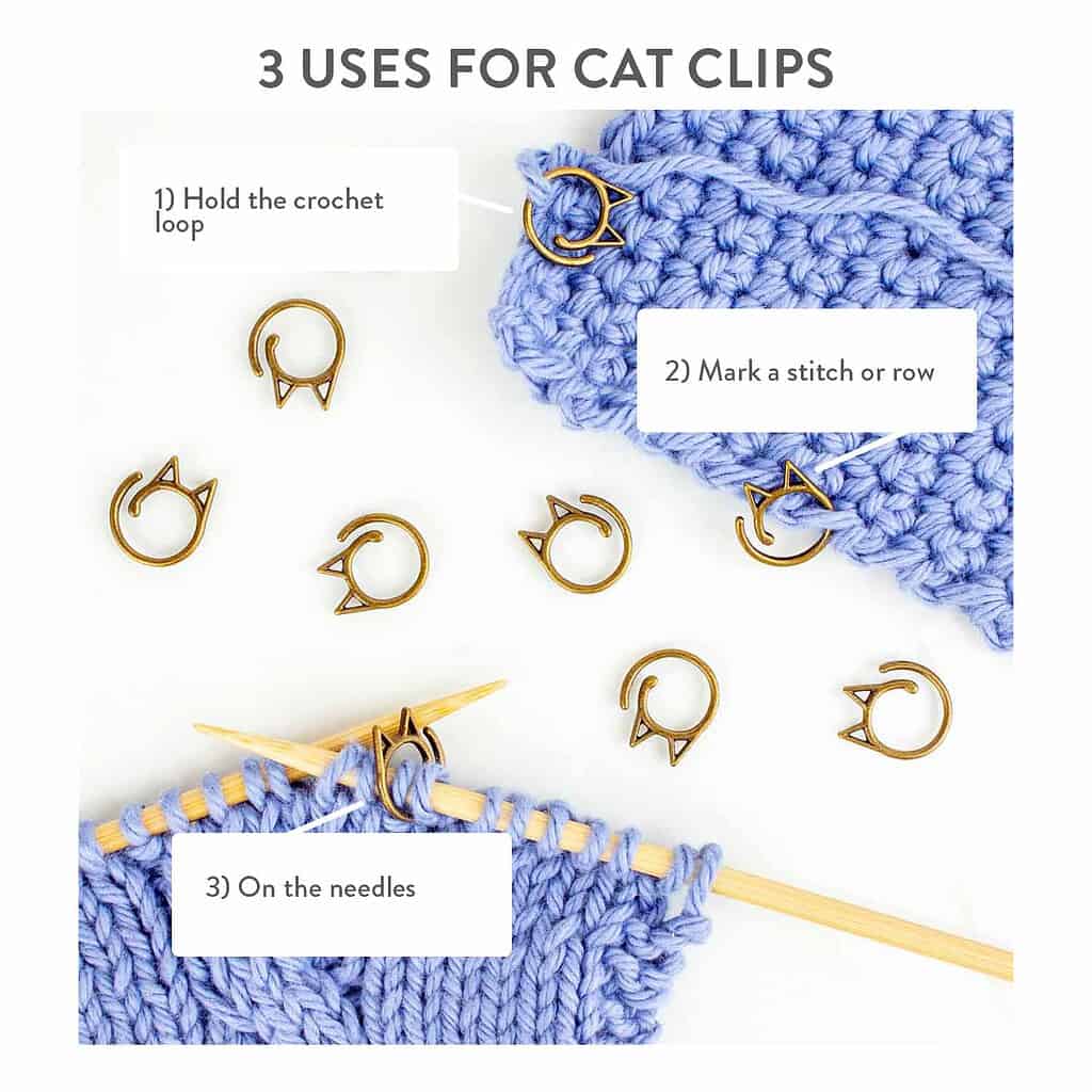 Blue yarn, wooden knitting needles, and gold cat stitch markers on a white background.