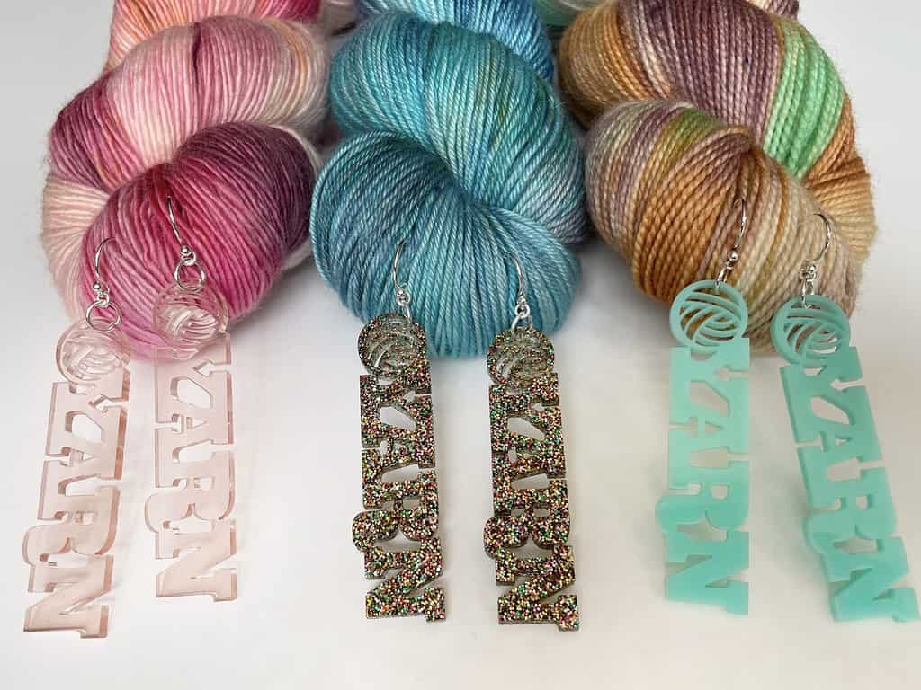 Glittery earrings in clear pink, multicolored glitter and aqua displays on yarn.