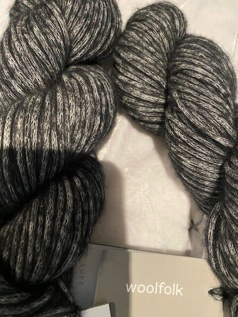 Two skeins of charcoal yarn with a Woolfolk tag.