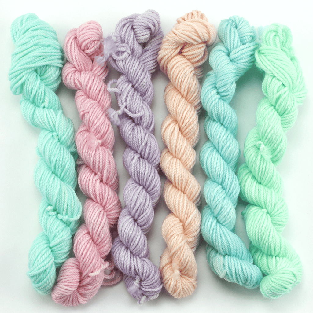 A set of six mini skeins of yarn in pastel colors.