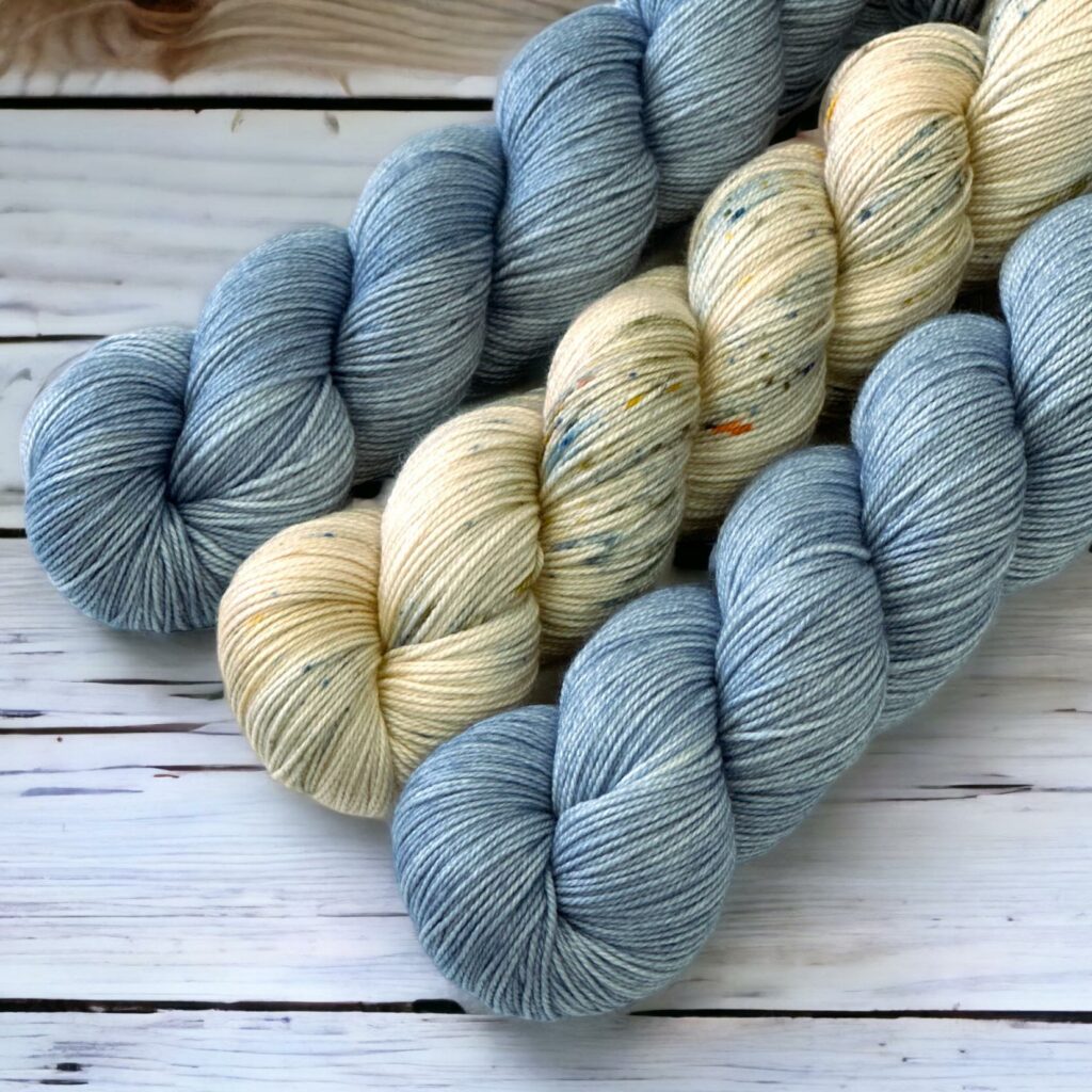 2 hanks of light blue yarn and speckled beige yarn.