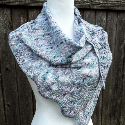 An aqua and lilac speckled lace shawl displayed on a dress form.