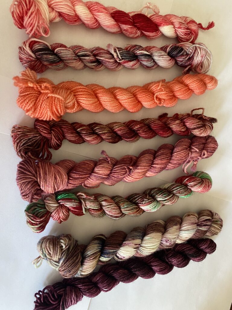 8 mini skeins of burgundy, pink and orange yarn.