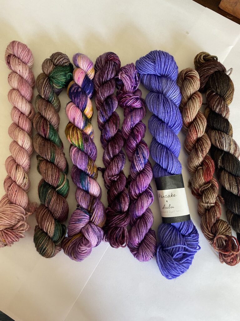 8 mini skeins of purple, pink, brown and green yarn.