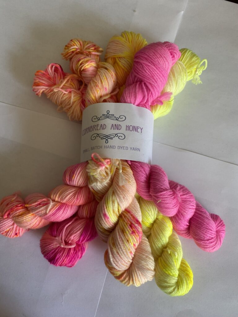 Five mini skeins of pink, orange, and yellow yarn.