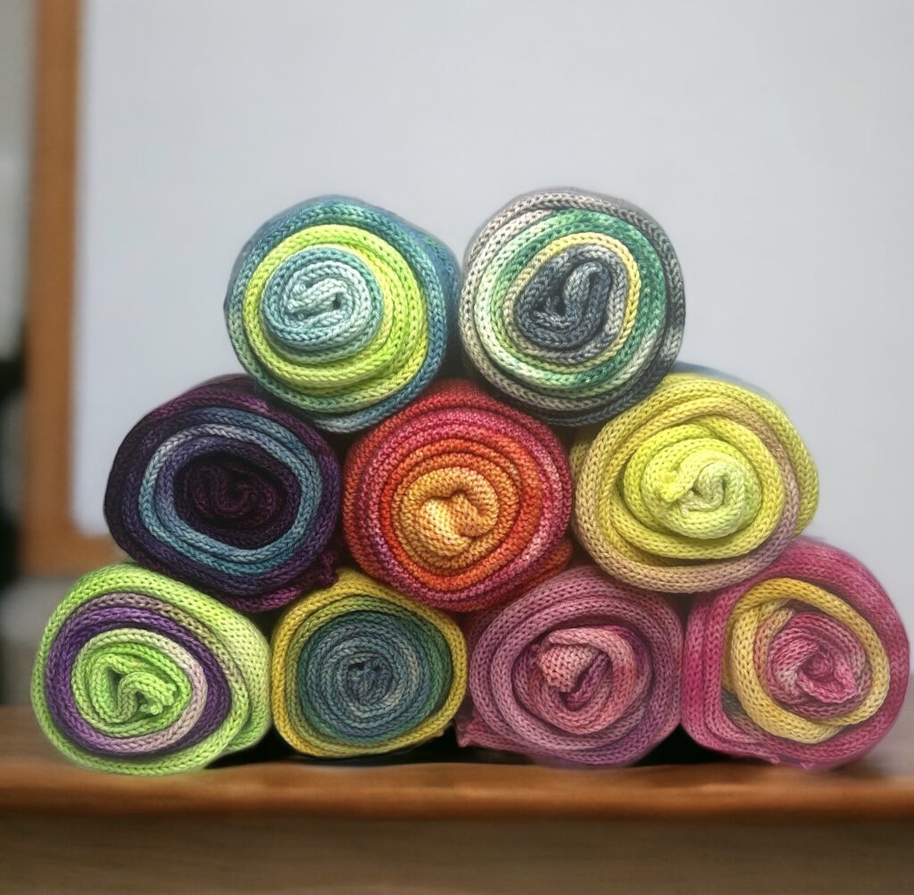 9 rolls of knitted fabric in various colors: blues, greens, reds, purples, pinks, yellows.