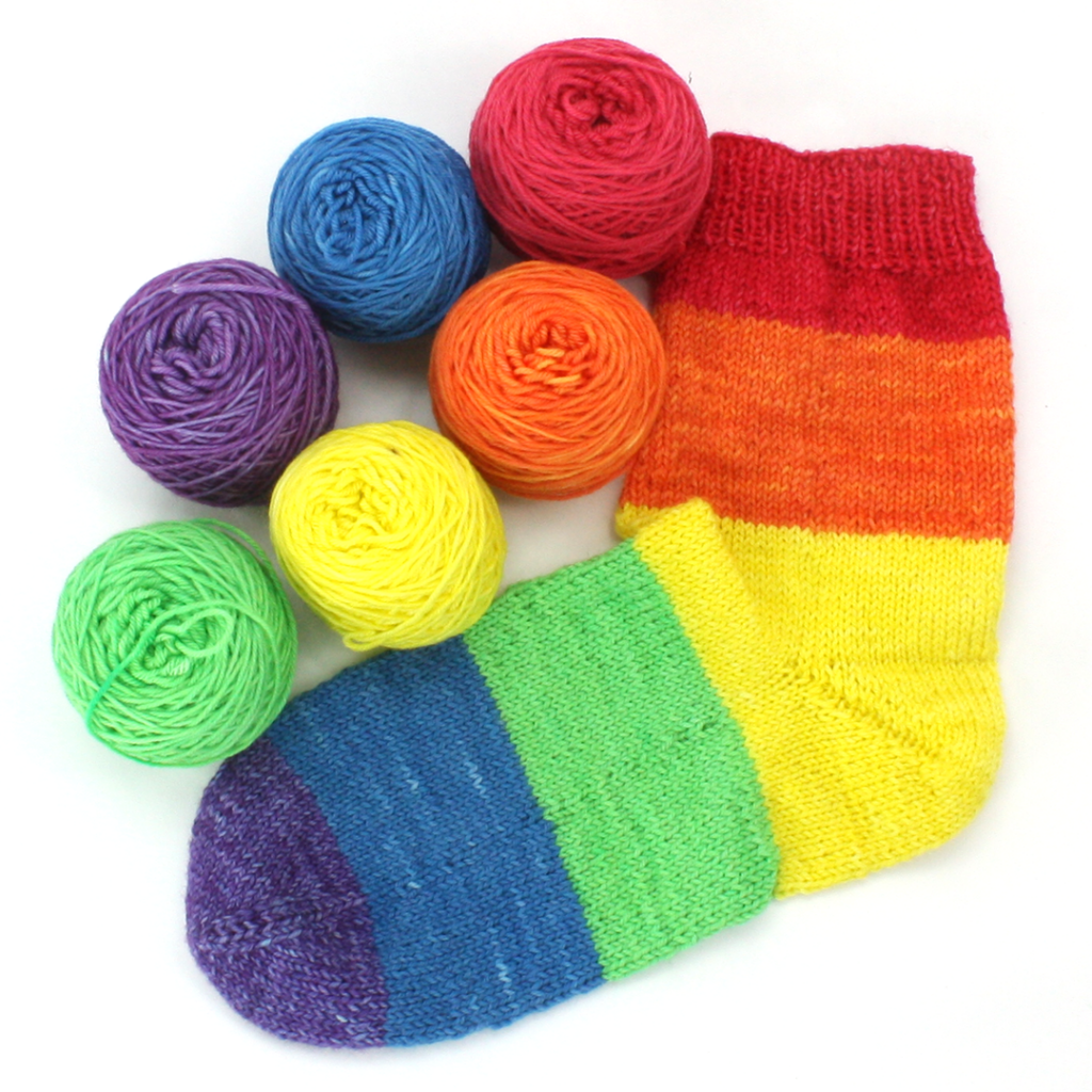 A sock knit with 6 rainbow colors surrounded by 6 rainbow balls of yarn.