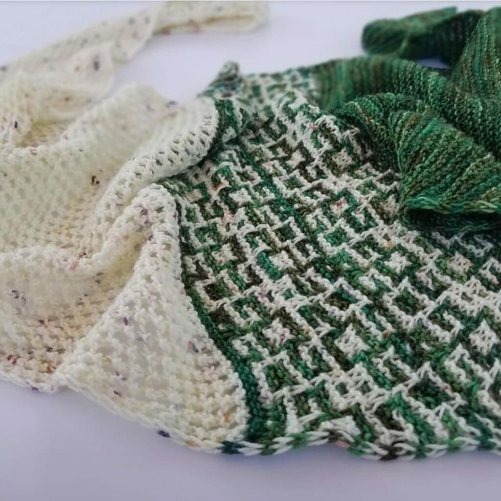 Triangular green and cream colored shawl with colorwork in the center, and simple lace on one end.