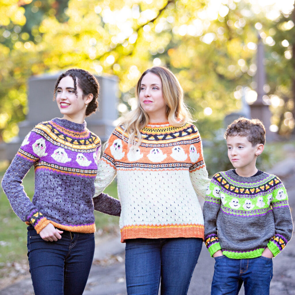 Three light-skinned people wearing hand knit halloween sweaters.