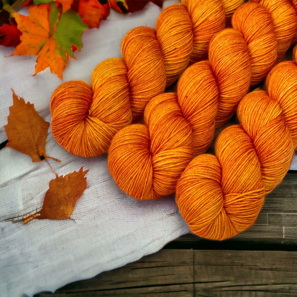 Three hanks of orange yarn on a cloth with autumn leaves.