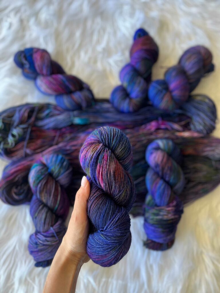 Deep blue and purple hand-dyed yarn and a light-skinned hand holding up a skein.