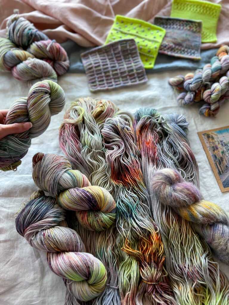 Gray yarn with bright blue, pink, purple and yellow. One twisted hank is held by a light-skinned hand. 