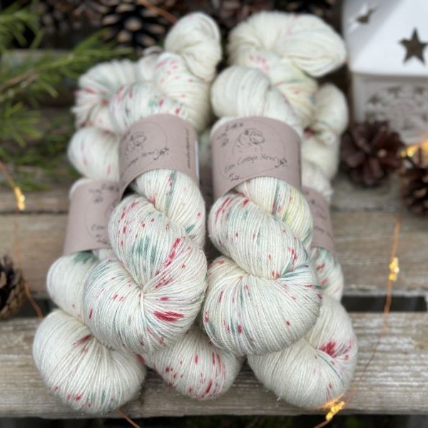 Five skeins of cream yarn with green and red speckles.