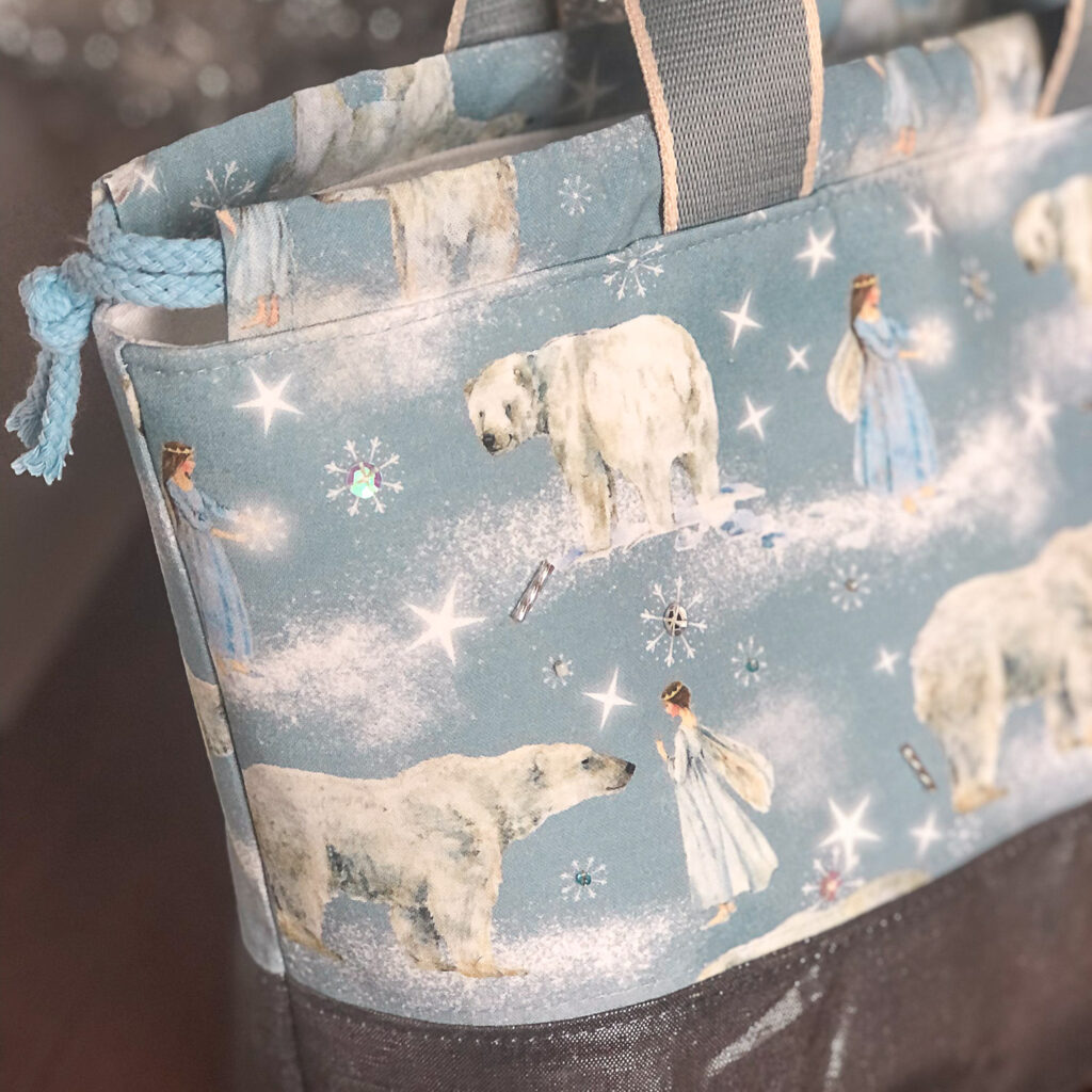 A close-up of a project bag with polar bear and angel fabric and beads.
