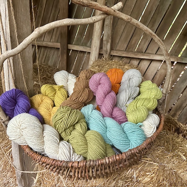 Large basket of yarns in varying colors, sitting on bale of straw.