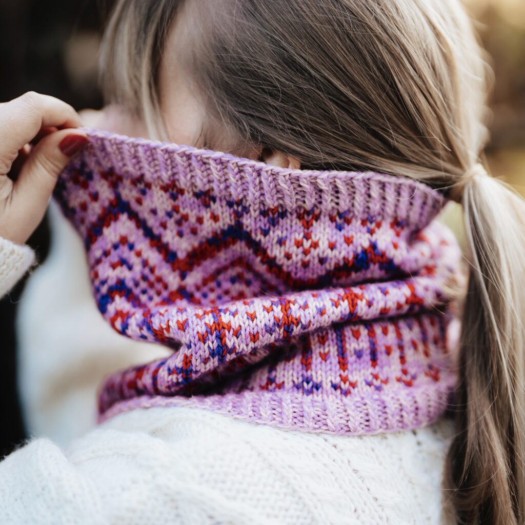 A colorwork cowl with pink, purple, red and blue.