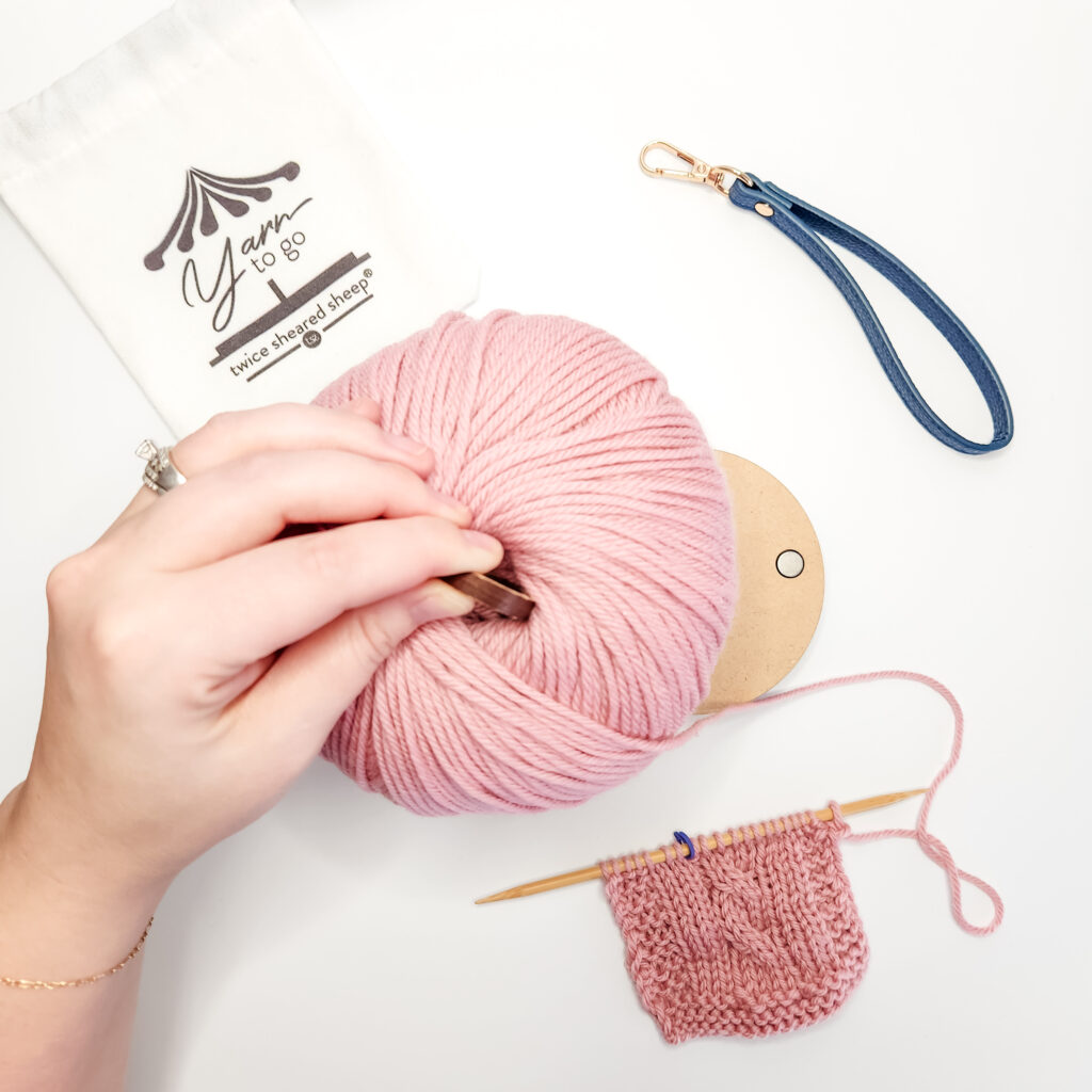 Pink skein of yarn on a brown yarn carousel with a white background and light-skinned hand.