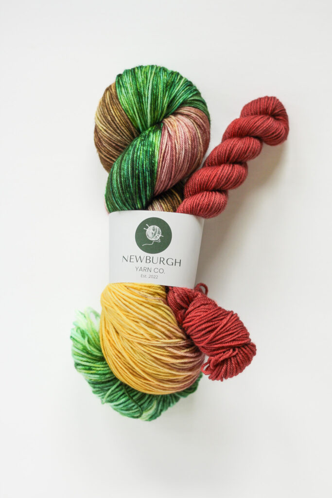 A sock set with green, yellow and red yarn and a red mini skein.