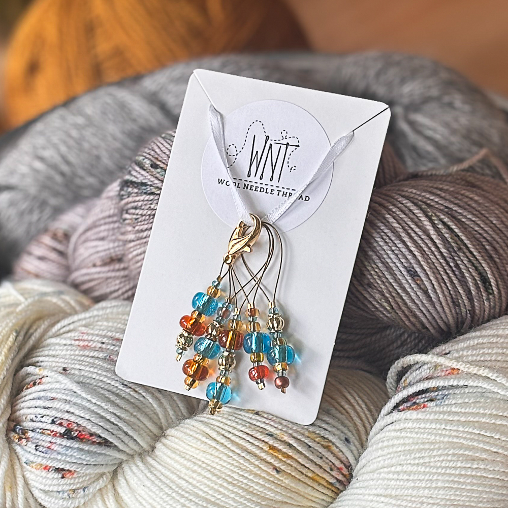 A set of blue and orange stitch markers standing in a bowl filled with yarn hanks.