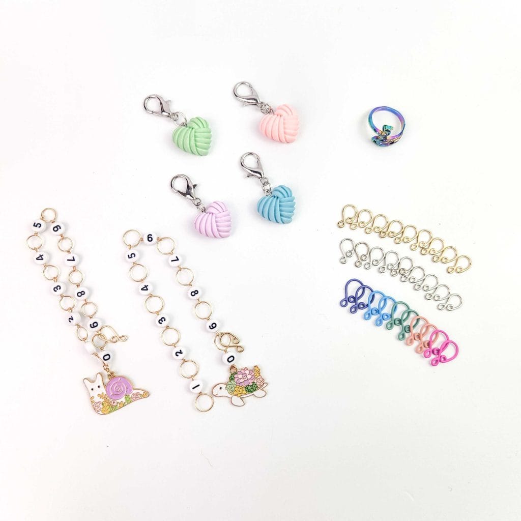 Green, pink, peach, blue and rainbow colored stitch markers and row counters on a white background.