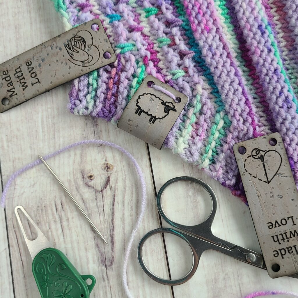 Grey cork tags on multicolored yarn with needle, scissors, and needle threader.