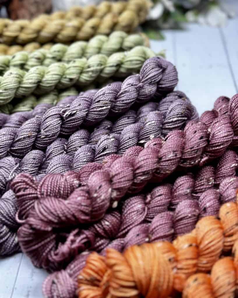 A selection of five different tonal color mini skeins, from orange, rose, purple, green and yellow, in muted, earthy tones.