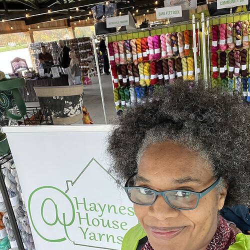 A Black woman standing in front of a booth of colorful yarn.