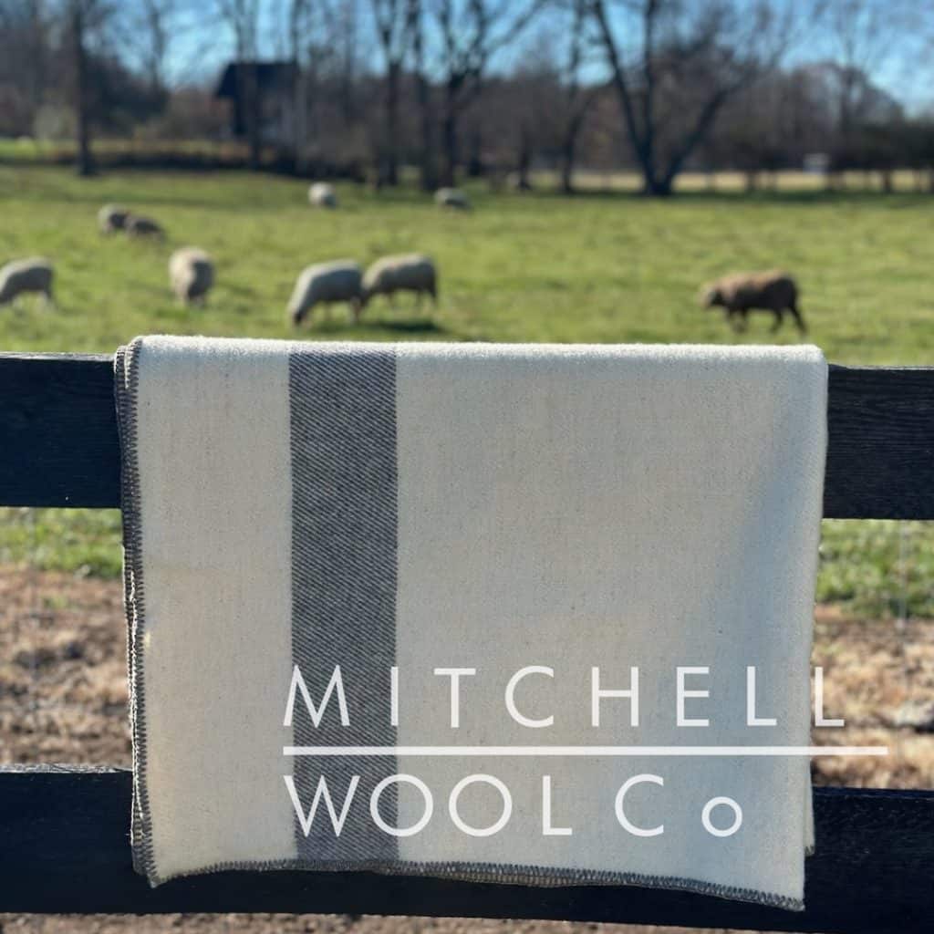 A white throw with a black stripe draped over a fence with sheep in the background.