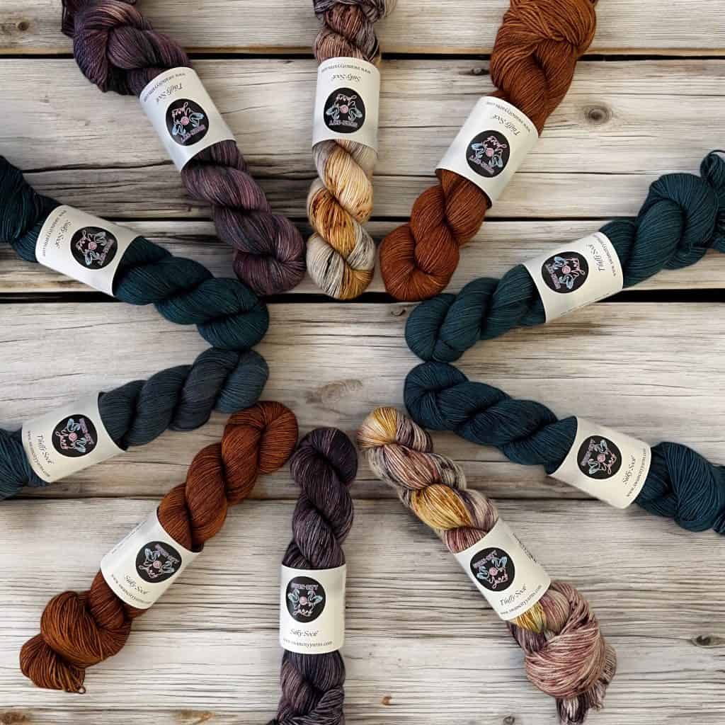 A circle formed of dark hand-dyed yarns in shades of purple, brown and teal extending outward.