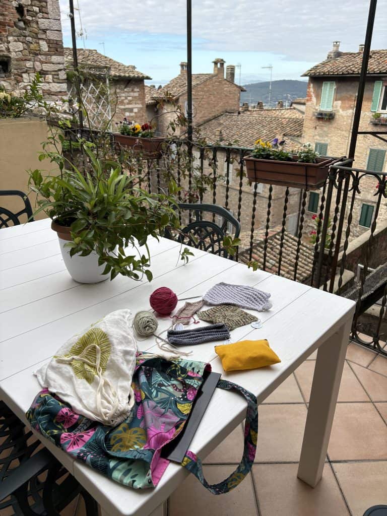 Table on a patio with knitting and yarn on it. Overlooking the buildings and hills of a town.