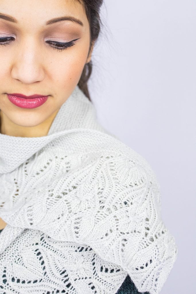 Close up shot of a woman's face looking down towards the white lace shawl wrapped gracefully around her neck.