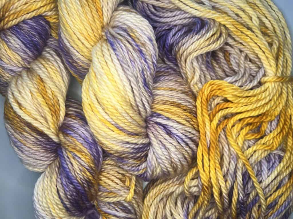 Three skeins of mustard yellow and purple yarn.