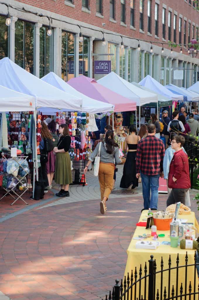 Outdoor fiber festival with vendor tents and shoppers.