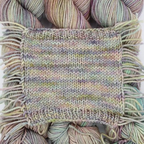 Five twisted skeins of yarn vertically lined up atop five skeins in the same colorways opened up and lined up horizontally